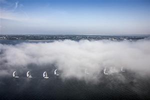 The fleet sailing downwind off the coast of Newport, with patches of fog rolling in photo copyright  Rolex/Daniel Forster http://www.regattanews.com taken at  and featuring the  class