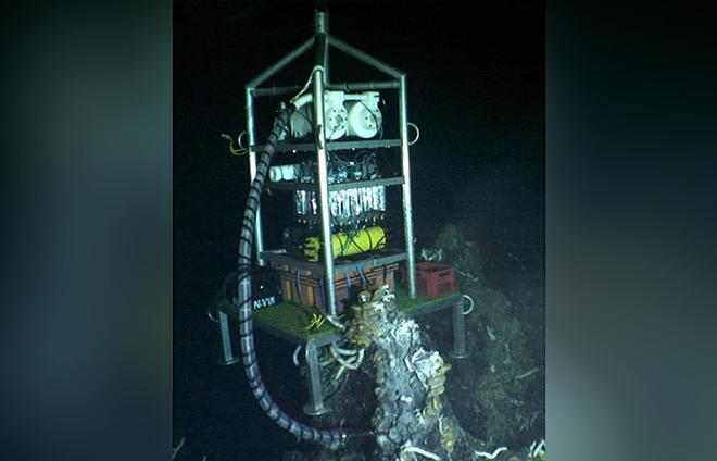 Vent-SID was deployed atop a vent site on the seafloor called Crab Spa. The Vent-SID collects fluid from the vent and incubates it in the white chambers near the top. Then it measures the rates at which microbes in the vent fluids perform chemosynthesis. © Chief Scientist Stefan Sievert WHOI