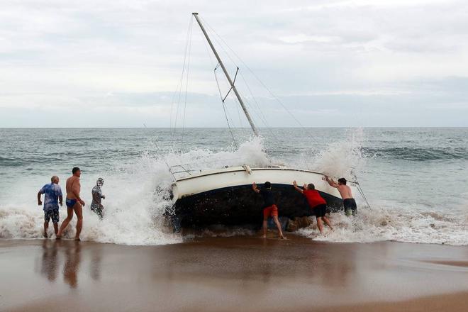 A group of bystanders attempt, unsuccessfully, to manoeuvre the yacht back into the water at Stanwell Park Beach on Sunday.  © Sylvia Liber