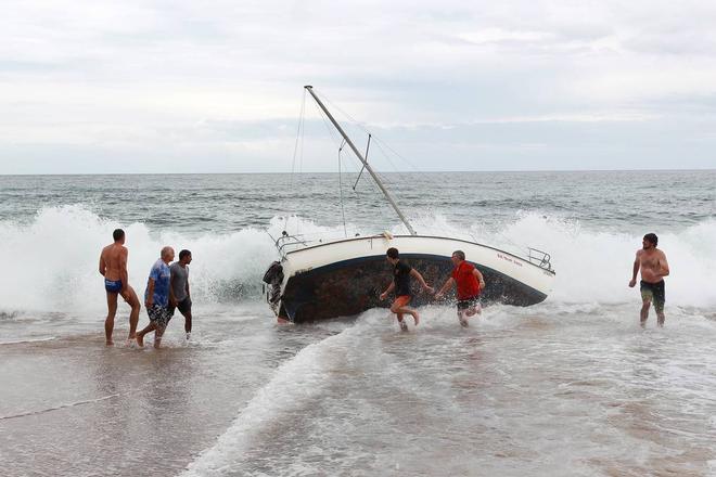 A group of bystanders attempt, unsuccessfully, to manoeuvre the yacht back into the water at Stanwell Park Beach on Sunday.  © Sylvia Liber