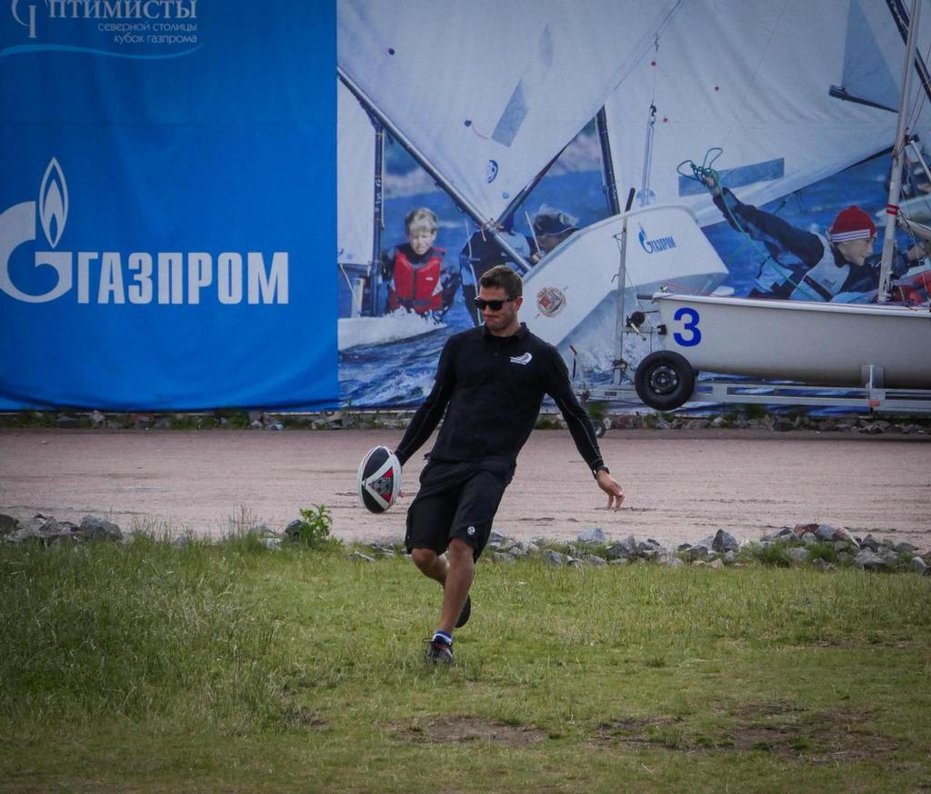 Blair Tuke kicks a rugby ball while waiting to launch the Extrem 40 yacht in St Petersburg Russia. © Hamish Hooper/Emirates Team NZ http://www.etnzblog.com
