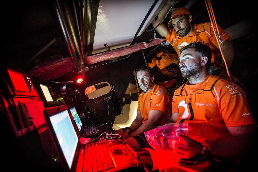 October 27, 2014. Leg 1 onboard Team Alvimedica. Day 16. The sky darkens as the progress south towards a low pressure system off Rio progresses; decision time for beginning the gradual turn east towards Cape Town. The brain-trust in the nav station: Will Oxley (L), Mark Towill (M), and Charlie Enright (R) dissect the latest weather information, crucial in determining the time to turn east for Cape Town. ©  Amory Ross / Team Alvimedica