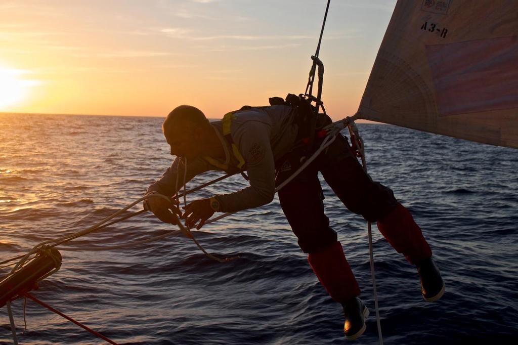 Leg 1 onboard Team Brunel, Gerd-Jan Poortman working on a sail, hanging by his harness only, at sunset. © Stefan Coppers/Team Brunel