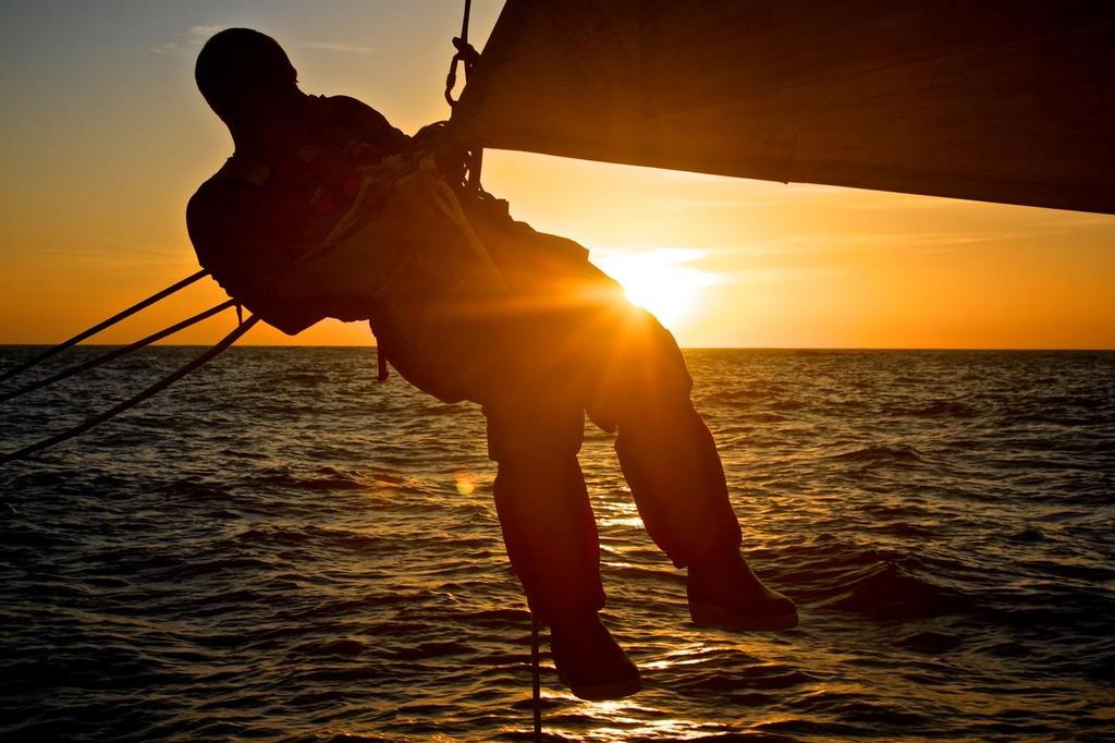 October 14, 2014. Leg 1 onboard Team Brunel, Gerd-Jan Poortman working on a sail, hanging by his harness only, at sunset. © Stefan Coppers/Team Brunel