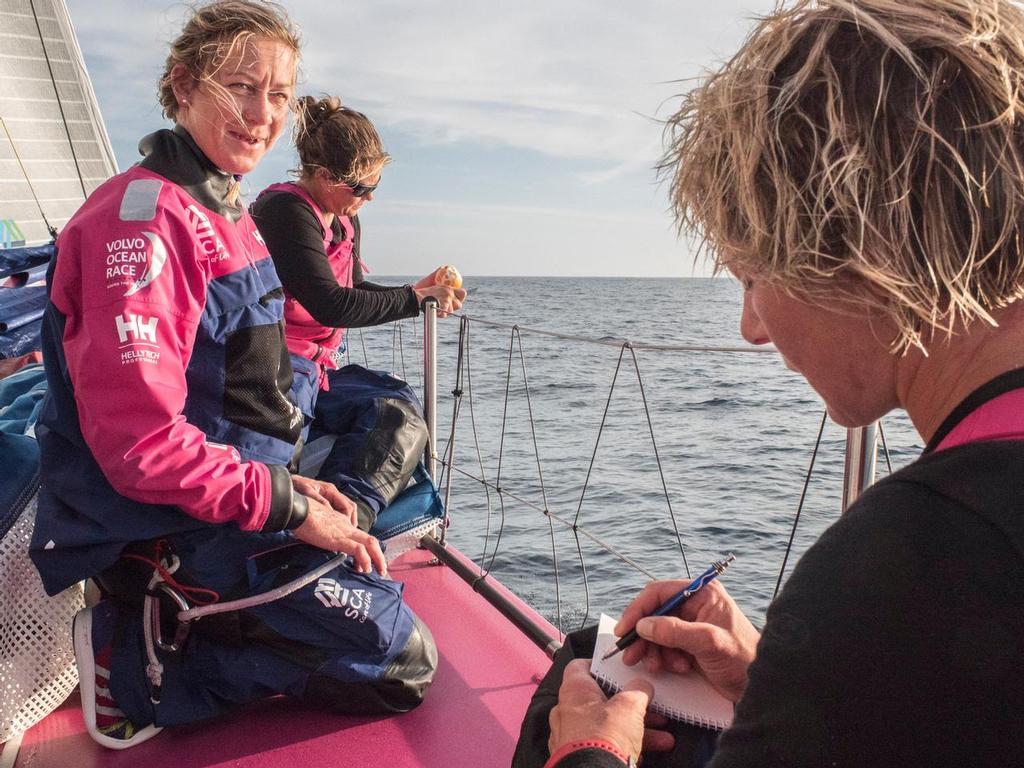 October 14, 2014. Leg 1 onboard Team SCA. Sally Barkow peals an orange to share while Abby makes some notes on things to fix on the boat. © Corinna Halloran / Team SCA