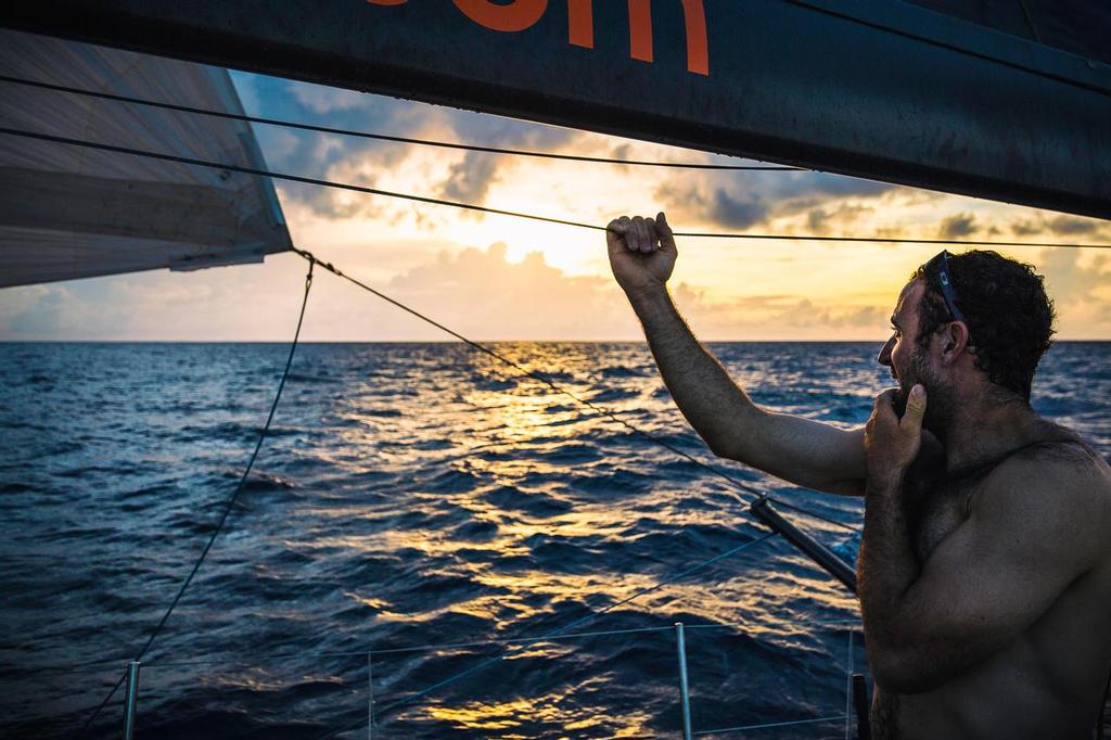 February 21, 2015. Leg 4 to Auckland onboard Team Alvimedica. Day 13. Seb Marsset looks to leeward where the sun just dipped below a rising cloud. Over the equator and back into the Southern Hemisphere, the weather turns tropical, rainclouds driving much of the day's direction south towards Vanuatu.  ©  Amory Ross / Team Alvimedica