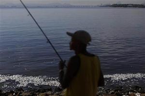 The Flavio Rodrigues, a retired rail worker, fishes on the shore of Guanabara Bay where dead fish float in Rio de Janeiro, Brazil, Wednesday, Feb. 25, 2015. Rio de Janeiroís state environmental agency is trying to determine why thousands of dead fish have been found floating where next yearís Olympic sailing events are to be held. photo copyright Leo Correa taken at  and featuring the  class