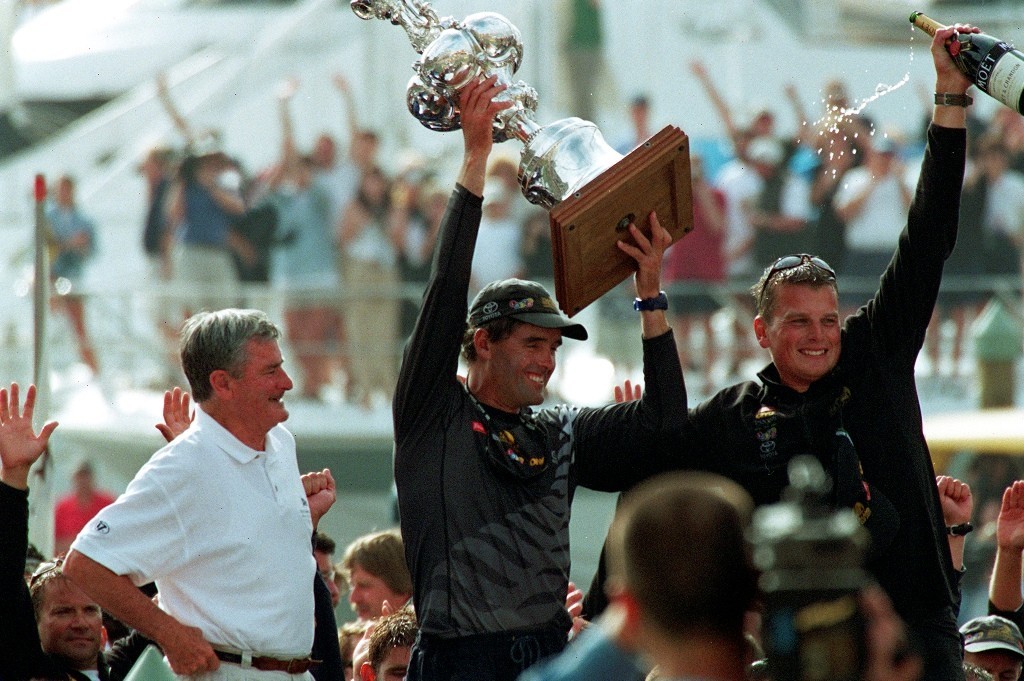 RNZYS Commodore Peter  Kingston looks on as Russell Coutts and Dean Barker celebrate with the America’s Cup after the 2000 defence.  © Event Media