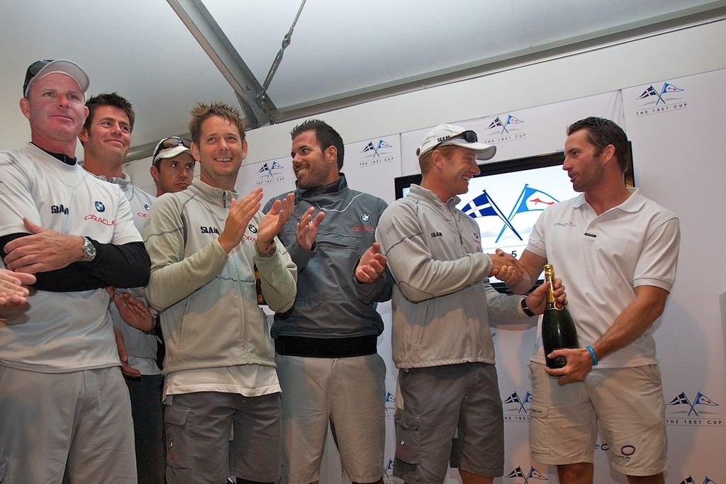 ENGLAND, Cowes, 6th August 2010. 1851 Cup Regatta. Day 4. Ben Ainslie, Skipper and Helm of TEAMORIGIN presents James Spittall, Skipper and Helm of BMW Oracle Racing with a bottle of champagne at the 1851 Cup Regatta prizegiving. © Ian Roman/TEAMORIGIN www.ianroman.com