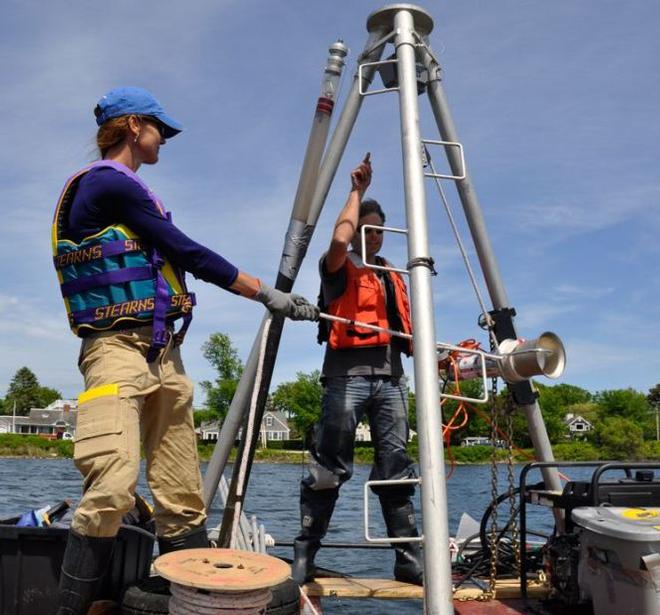 Working from a pontoon platform, the research team collected a sediment core from Salt Pond in Falmouth, Mass. An aluminum tube was vibrated through the metal tripod into the muddy sediment at the bottom of the pond and then extracted with a hoist. The core provides evidence of intense storm events going back approximately 2000 years - Prehistoric-hurricanes © WHOI Archives