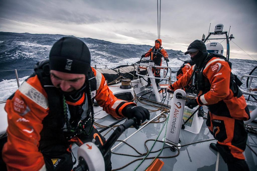 March 24, 2015. Leg 5 to Itajai onboard Team Alvimedica. Day 6. A late night gybe set off a wild day of true Southern Ocean sailing as the temps dropped and the wind and waves built with an approaching low pressure system and accompanying cold front. Ryan Houston driving in strong winds and Southern Ocean waves, while Charlie Enright (L) and Dave Swete (R) shake a reef on the mainsail. ©  Amory Ross / Team Alvimedica