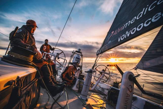 Leg 7 to Lisbon onboard Team Alvimedica. Day 03. The sun goes down behind Alberto Bolzan (driving),Dave Swete (L),and Seb Marsset (R),giving way to a cold night in the North Atlantic. Approaching the southern limits of the Greenland Ice Exclusion Zone the fleet compresses further,all six within sight of each other. - Volvo Ocean Race 2015 ©  Amory Ross / Team Alvimedica