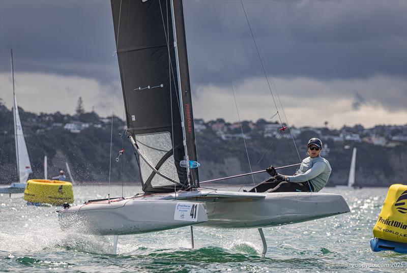 PredictWind A-Class Cat Worlds 2025 - Kiwi lad, Hamish Hall-Smith, looks to have got his sail shape fixed finally photo copyright Gordon Upton / www.guppypix.com taken at Milford Cruising Club and featuring the A Class Catamaran class