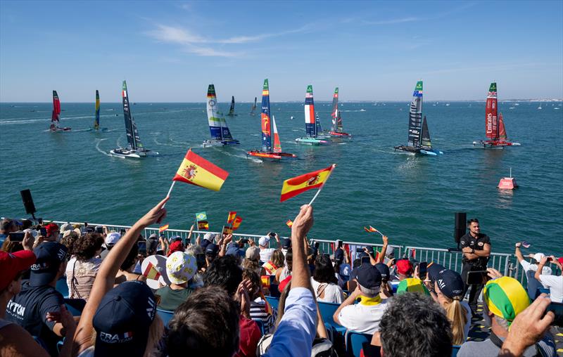 Spectators wave their flags as they watch the action from the grandstand in the race stadium as Emirates Great Britain SailGP Team lead ahead of New Zealand SailGP Team, Spain SailGP Team and the fleet on Race Day 1 of the DP World Spain Sail Grand Prix - photo © Andrew Baker for SailGP