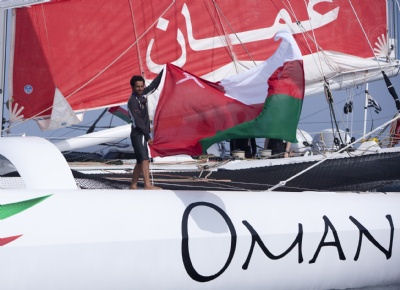 Mohsin Ali Al Busaidi flies the Omani flag after crossing the finish line in Muscat and making history photo copyright Lloyd Images / Oman Sail taken at  and featuring the Maxi Cat class