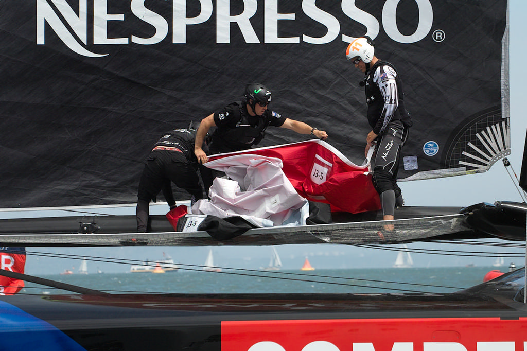 Black helmeted shore support crews help with pre-race prep on the way to the course.  - America’s Cup © Chuck Lantz http://www.ChuckLantz.com