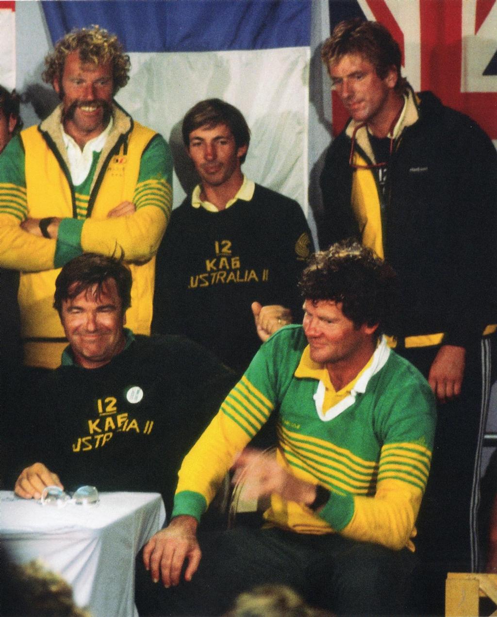 Seated from left, Ben Lexcen lets the moment of Australia II’s victory sink in, while to the right, John Longley has a few comments for the media. Longley was project manager and grinder on Australia II © Maritime Productions LLC http://www.maritimeproductions.tv/