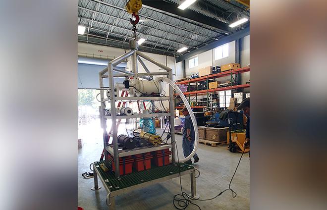 WHOI microbiologist Craig Taylor and a team of WHOI engineers designed and built Vent-SID, shown here in the high bay in the Rinehart Coastal Reseach Center at WHOI. Orange battery packs heat twin chambers to the temperatures of fluid emanating from hydrothermal vents. The long clear tube has a nozzle to suck vent fluids into test chambers.  © Fred Thwaites WHOI