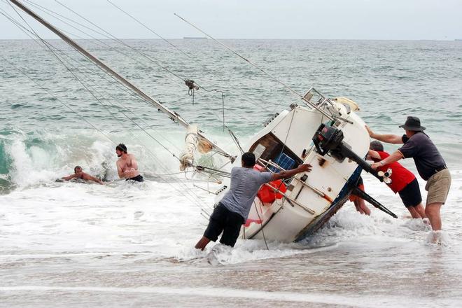 A group of bystanders attempt, unsuccessfully, to manoeuvre the yacht back into the water at Stanwell Park Beach on Sunday.  © Sylvia Liber