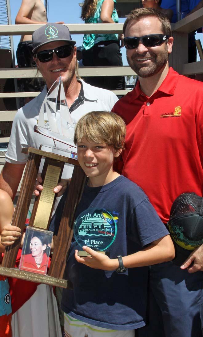 TJ O'Rourke of Dana Point Yacht Club proudly holds the Jessica Uniack Memorial Beach to Bay Race perpetual trophy after finishing first in the Sabot C3 class in the 2014 Beach to Bay Race. Long Beach Yacht Club Sailing Director Jess Gerry (left) and son of Jessica Uniack, Alex Uniack (right), congratulate TJ on his win. The trophy is traditionally awarded to the first place finisher in the largest class. © Rick Roberts