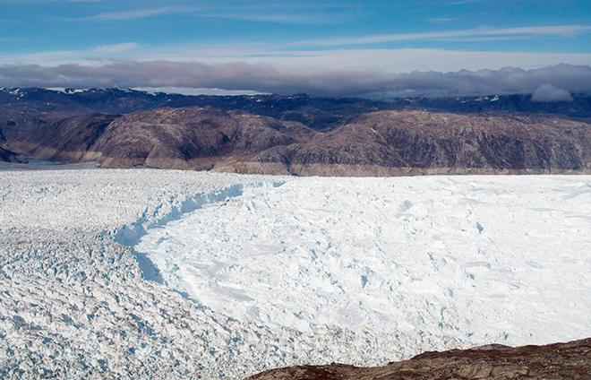 The ridge of ice is the terminus of Helheim Glacier, where it flows into the ocean. To the right of the ridge, the fjord is covered by a thick melange of floating icebergs and sea ice. That makes the region near the glacier's terminus inaccessible by boat. On the mountains in the background, you can see a 