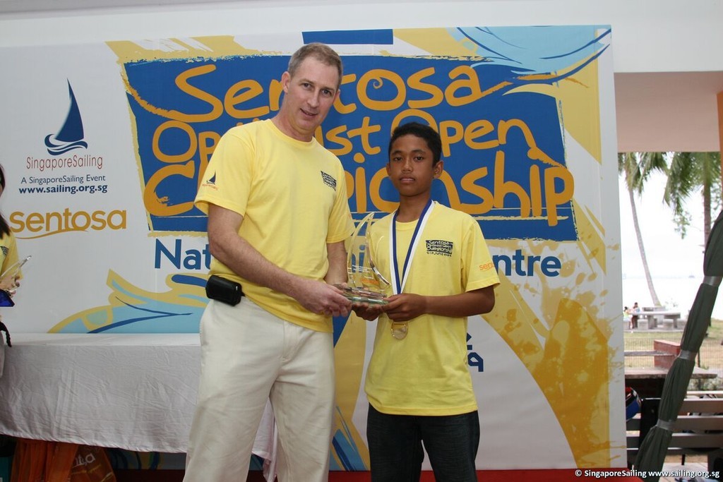Mohamad Faizal B Norisah (MAS) receiving the Sentosa Optimist Open Championship Challenge Trophy from Mr Andrew Sanders, CEO of SingaporeSailing (left). <br />
  © SingaporeSailing