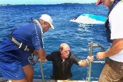 Men rescued: Mitchell DeShields and Dylan Clark, crew members of the Spirit of Bermuda, pull onboard one of two men the sloop rescued when their boat capsized. The other man can be seen next to the distressed boat, off St George's, Sunday afternoon. photo copyright SW taken at  and featuring the  class