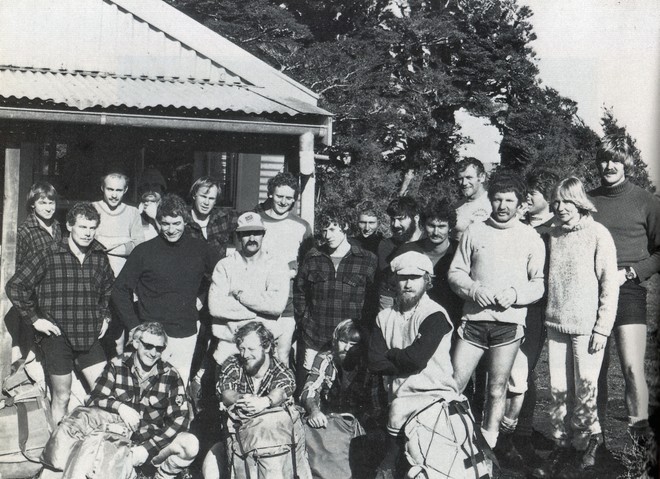September 1980: Martin Foster (lower left in checked shirt and sunglasses) on the tramp in the Urewera’s used for final crew selection in the Ceramco campaign. Grant Dalton (dark checked shirt and shorts is immediately behind Foster). Chris Dickson (blonde curly hair) is at the back beside the shed wall. Geoff Stagg is on the left of Peter and Pippa Blake (extreme right). © SW