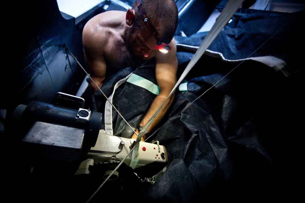 A domesticated Ryan Godfrey at work repairing a ripped sail with the onboard sewing machine. © Amory Ross/Puma Ocean Racing/Volvo Ocean Race http://www.puma.com/sailing
