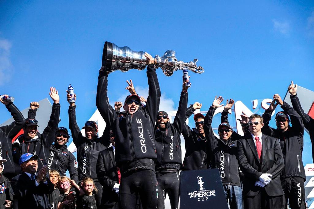 San Francisco (USA CA) September 25th, Race day 15 of the 34th America's Cup racing between Oracle Team USA skippered by James Spithill (AUS) and Emirates Team New Zealand skippered by Dean Barker (NZL). Oracle Team USA wins the America's Cup in the final race after winning nine straight races. Team celebrates with champagne on board. Dock side Sir Ben Ainslie holds trophy over his head as team cheers. photo copyright Bob Grieser/Outside Images www.outsideimages.com taken at  and featuring the  class