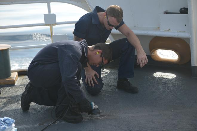 Seaman Gannon instructs a newly reported shipmate on the proper way to use power tools while removing rust spots from the deck of Coast Guard cutter Active on Oct. 11, 2017. Coast Guard cutter Active is homeported in Port Angeles, Washington. © Petty Officer 3rd Class Nicole J. Groll
