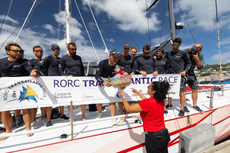 Grenada Tourism Authority representative Alyssa Bierzynski presenting a gift basket of Grenadian goods - 2023 RORC Transatlantic Race photo copyright Arthur Daniel / RORC taken at Royal Ocean Racing Club and featuring the Volvo 70 class